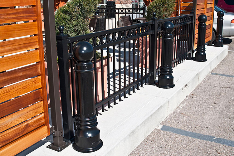 Fences and bollards often work together: here, security bollards protect a wrought iron fence.